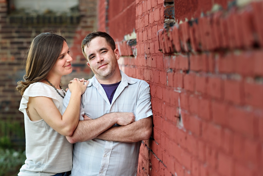 An adorable couple leaning against a red brick wall in fishtown.